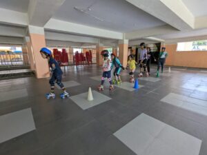 Children wearing helmets and roller skates practicing indoors, navigating around cones on a tiled floor.